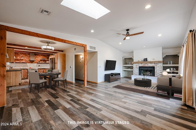 living room with ceiling fan, vaulted ceiling with skylight, built in features, and hardwood / wood-style flooring