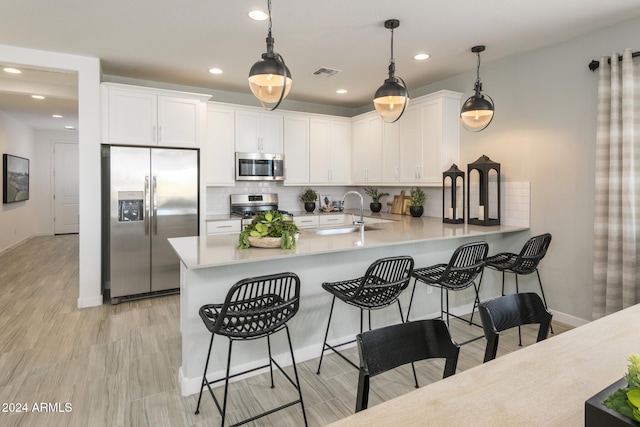 kitchen with sink, hanging light fixtures, appliances with stainless steel finishes, kitchen peninsula, and white cabinets