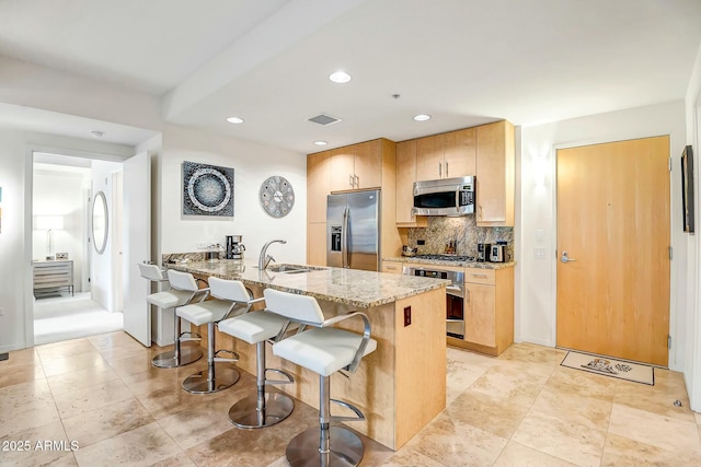 kitchen featuring visible vents, light stone counters, a kitchen breakfast bar, stainless steel appliances, and a sink