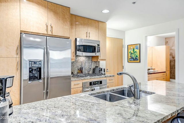 kitchen with decorative backsplash, appliances with stainless steel finishes, light stone counters, and a sink