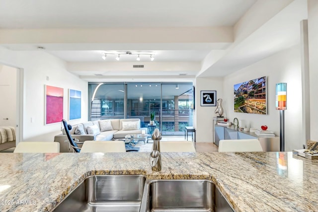 kitchen with visible vents, light stone counters, open floor plan, and a sink