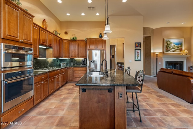 kitchen featuring a breakfast bar area, tasteful backsplash, dark stone countertops, stainless steel appliances, and a kitchen island with sink