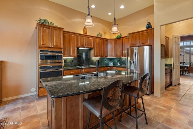 kitchen featuring sink, tasteful backsplash, dark stone countertops, a towering ceiling, and a kitchen island with sink