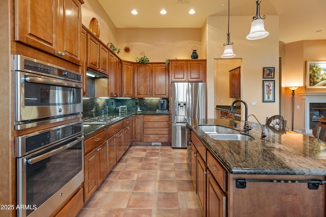 kitchen with an island with sink, sink, decorative backsplash, hanging light fixtures, and stainless steel appliances