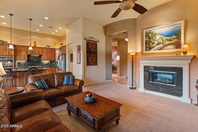 living room with ceiling fan, light colored carpet, sink, and a towering ceiling