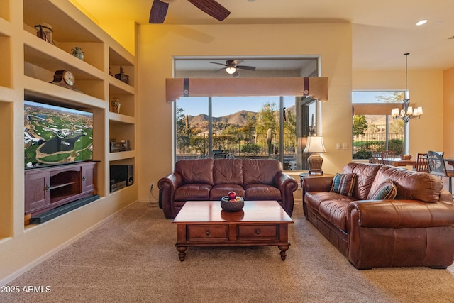 carpeted living room with built in shelves, plenty of natural light, a mountain view, and ceiling fan with notable chandelier