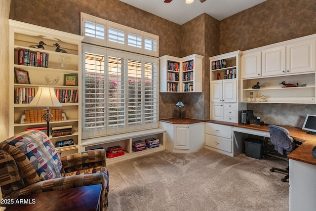 home office with light carpet, a towering ceiling, built in desk, and ceiling fan