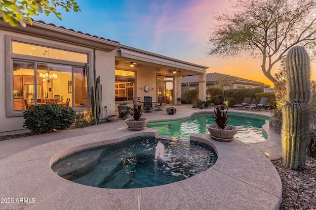 pool at dusk with a patio, ceiling fan, and an in ground hot tub