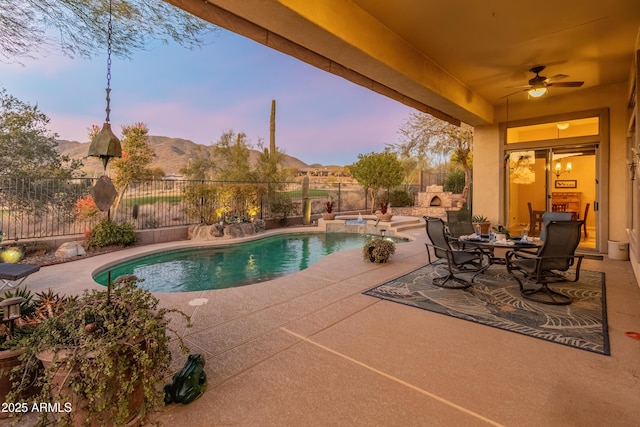 pool at dusk featuring a mountain view, a patio, and ceiling fan