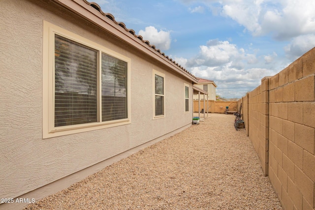 view of side of property featuring a tile roof, a fenced backyard, and stucco siding