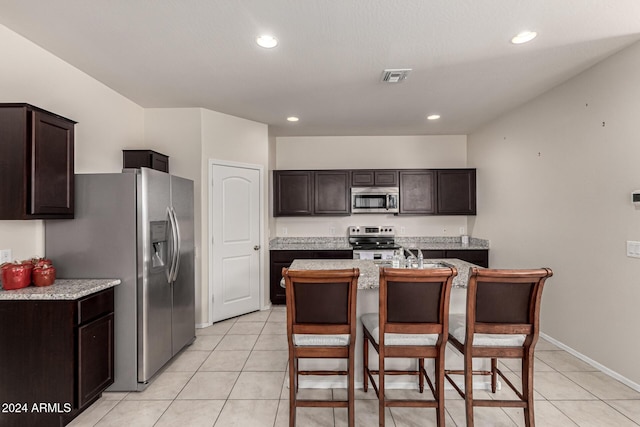 kitchen featuring dark brown cabinets, light tile patterned floors, stainless steel appliances, and a center island with sink