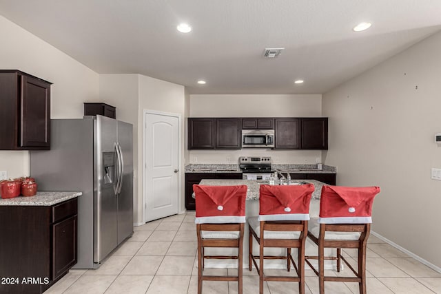 kitchen with light tile patterned flooring, appliances with stainless steel finishes, dark brown cabinets, and a kitchen island with sink