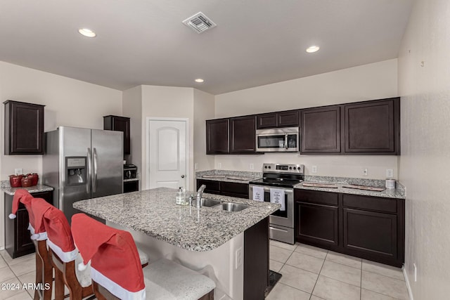 kitchen with a kitchen island with sink, sink, dark brown cabinets, light tile patterned flooring, and stainless steel appliances