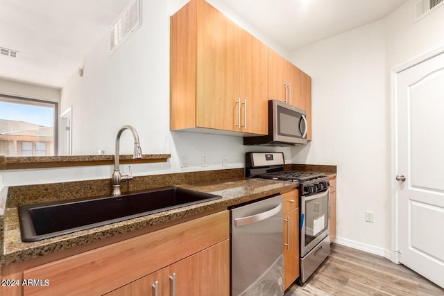 kitchen featuring stainless steel appliances, light hardwood / wood-style flooring, dark stone counters, and sink