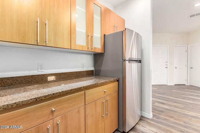 kitchen with stone counters, stainless steel fridge, and light hardwood / wood-style flooring