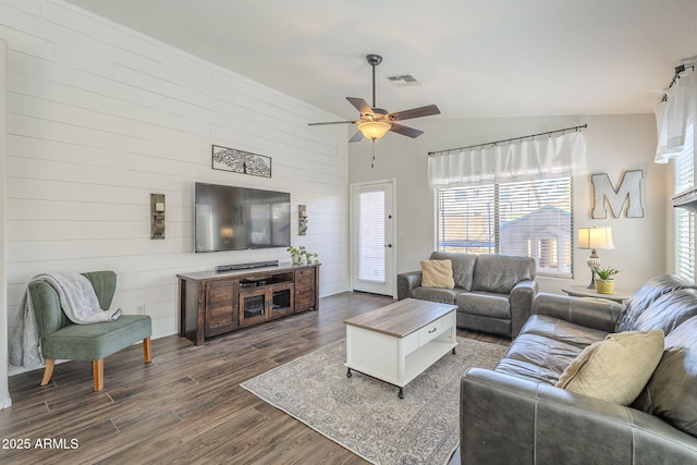 living room with ceiling fan, wooden walls, and vaulted ceiling