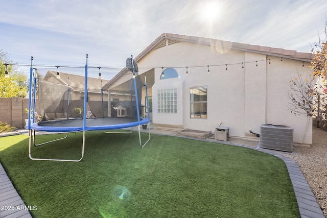 back of property featuring a trampoline, cooling unit, and a lawn