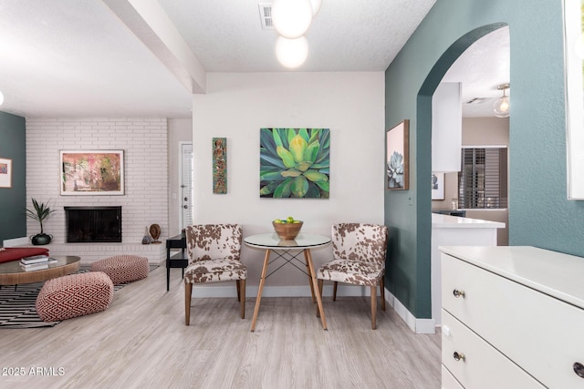 sitting room featuring arched walkways, a fireplace, baseboards, and light wood-style floors