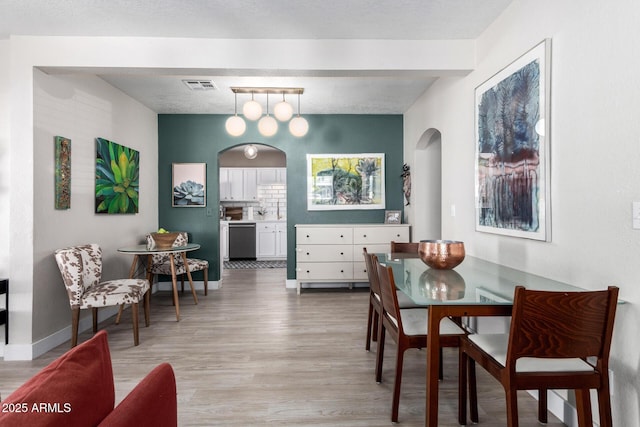 dining area featuring arched walkways, visible vents, light wood finished floors, and baseboards