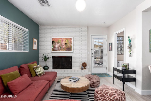 living room with a brick fireplace, baseboards, visible vents, and light wood finished floors