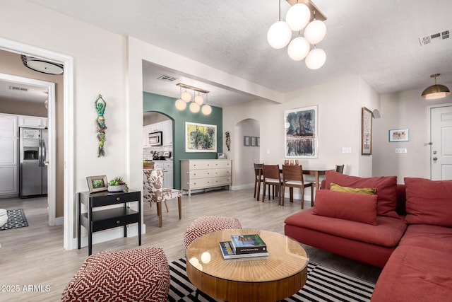 living room with baseboards, visible vents, arched walkways, light wood-style floors, and a textured ceiling