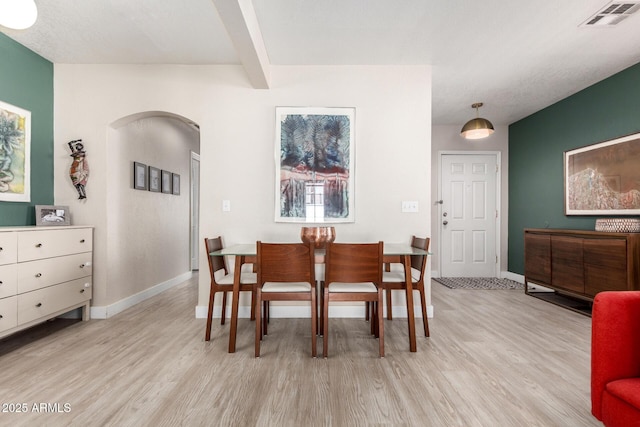 dining space with beam ceiling, arched walkways, visible vents, and light wood-type flooring