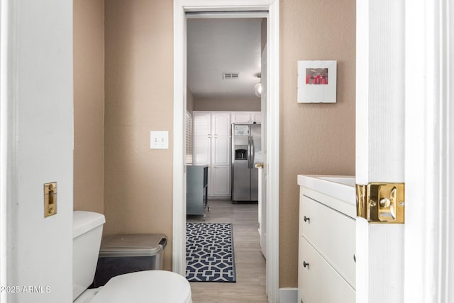 half bath with visible vents, toilet, wood finished floors, and a textured wall