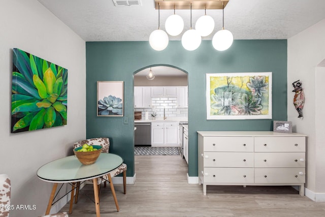 dining area with visible vents, baseboards, arched walkways, light wood-style floors, and a textured ceiling