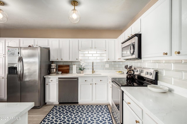 kitchen with light wood-type flooring, decorative backsplash, stainless steel appliances, white cabinetry, and a sink