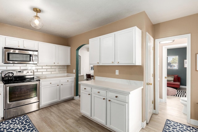 kitchen featuring arched walkways, white cabinets, stainless steel appliances, and light wood-style floors