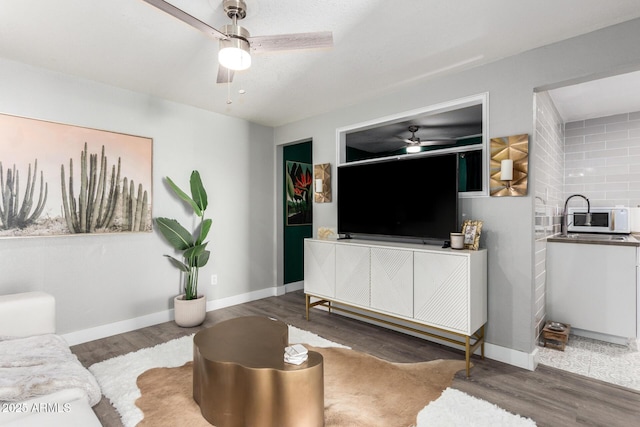 living area with a ceiling fan, wood finished floors, and baseboards