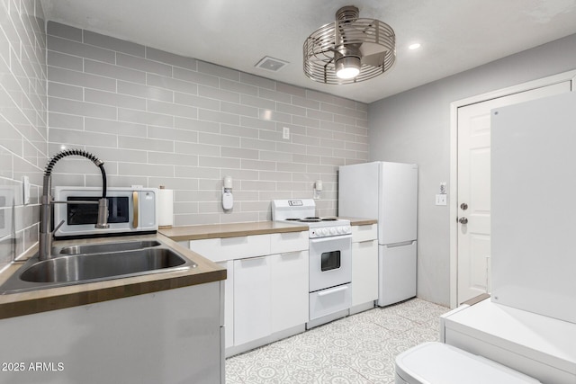 kitchen featuring tasteful backsplash, visible vents, white appliances, white cabinetry, and a sink