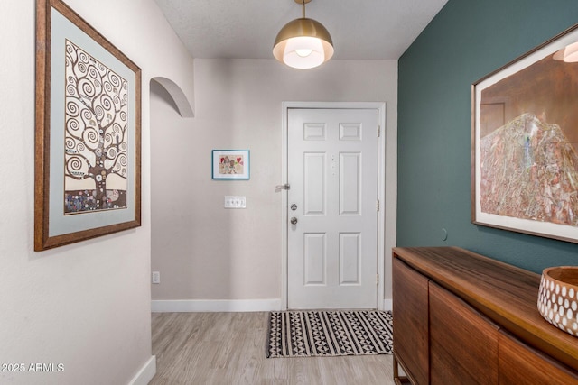 entrance foyer with baseboards, arched walkways, and light wood finished floors