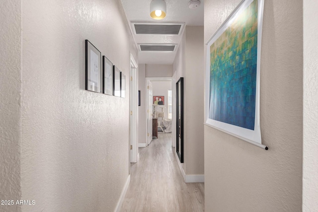 hall featuring wood finished floors, visible vents, and a textured wall