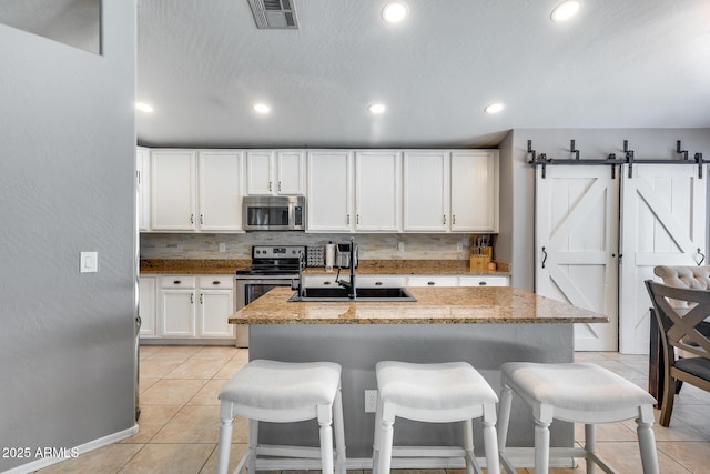 7435 W Trails Dr, Glendale, AZ 85308 - kitchen featuring stainless steel appliances, light tile patterned floors, white cabinetry, a kitchen breakfast bar, and decorative backsplash