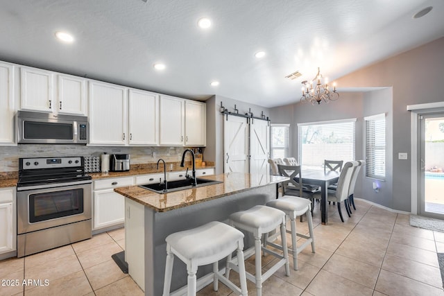 7435 W Trails Dr, Glendale, AZ 85308 - kitchen with appliances with stainless steel finishes, a barn door, decorative backsplash, light tile patterned floors, and healthy amount of natural light
