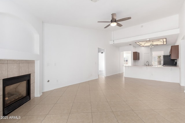 unfurnished living room with light tile patterned flooring, lofted ceiling, sink, ceiling fan, and a tiled fireplace