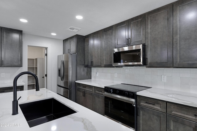 kitchen featuring sink, light stone countertops, tasteful backsplash, dark brown cabinetry, and stainless steel appliances