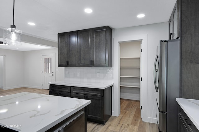 kitchen featuring light stone counters, stainless steel fridge, pendant lighting, decorative backsplash, and light wood-type flooring