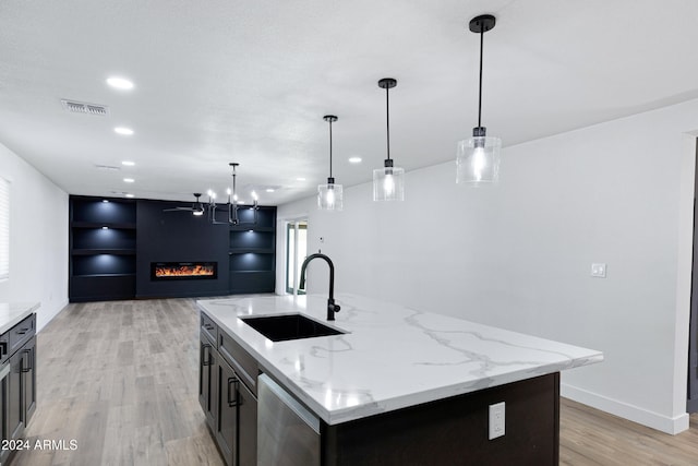 kitchen with light stone countertops, light wood-type flooring, a kitchen island with sink, sink, and pendant lighting