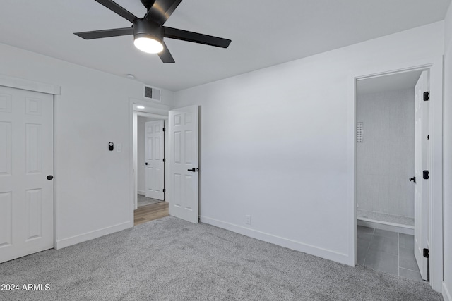 unfurnished bedroom featuring ceiling fan, a closet, light colored carpet, and ensuite bath