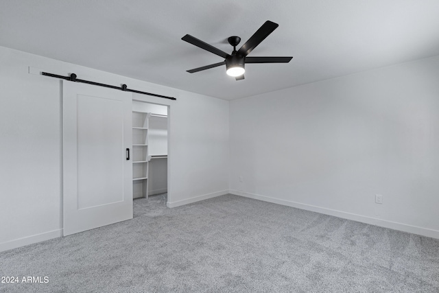 unfurnished bedroom with a barn door, light colored carpet, a spacious closet, and ceiling fan