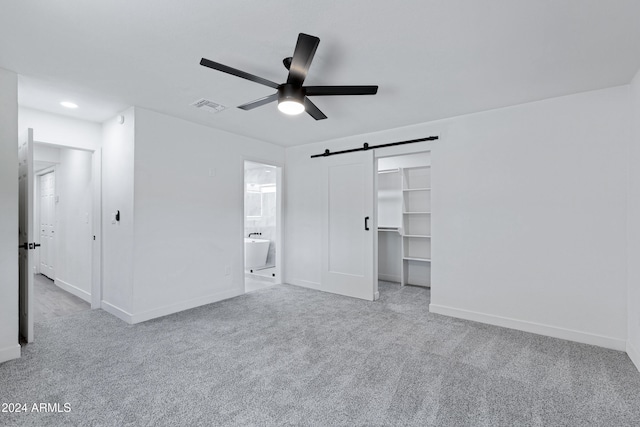 unfurnished bedroom featuring ensuite bathroom, light colored carpet, ceiling fan, a barn door, and a closet