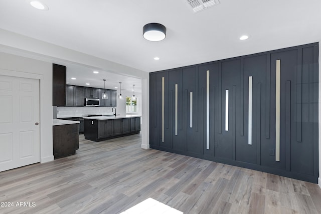 kitchen featuring backsplash, sink, hanging light fixtures, an island with sink, and light hardwood / wood-style floors