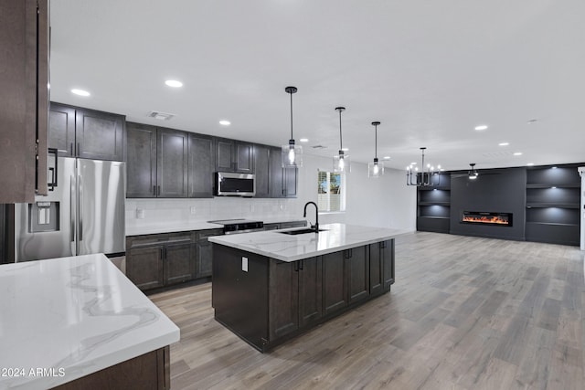 kitchen with sink, light stone counters, decorative light fixtures, appliances with stainless steel finishes, and light wood-type flooring