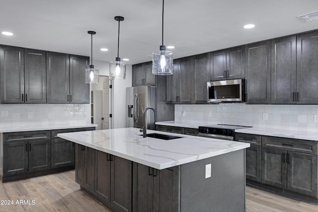 kitchen with a kitchen island with sink, sink, light hardwood / wood-style floors, and appliances with stainless steel finishes