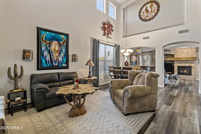 living room with a high ceiling, hardwood / wood-style flooring, a chandelier, and a stone fireplace