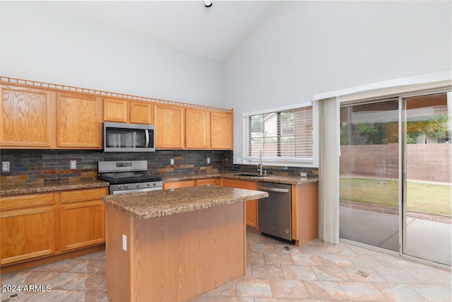 kitchen with high vaulted ceiling, dark stone counters, sink, appliances with stainless steel finishes, and a kitchen island