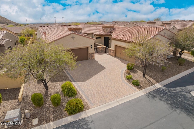 view of front of house featuring stucco siding, decorative driveway, stone siding, an attached garage, and a tiled roof