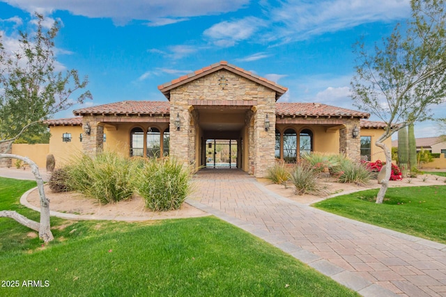 mediterranean / spanish home with stone siding, stucco siding, a tiled roof, and a front lawn